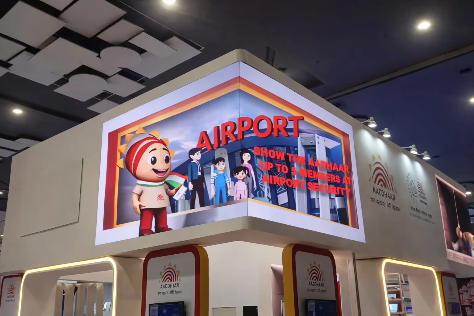 Digital display at an Aadhaar booth showing a cartoon character holding an Indian flag and text advising to show Aadhaar for up to five