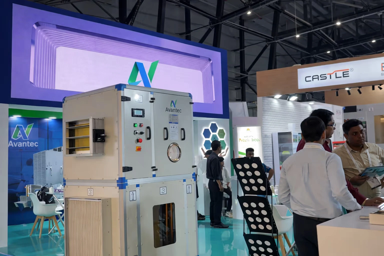 Exhibition booth featuring a large Avantec branded industrial machine with people engaging in discussions nearby.