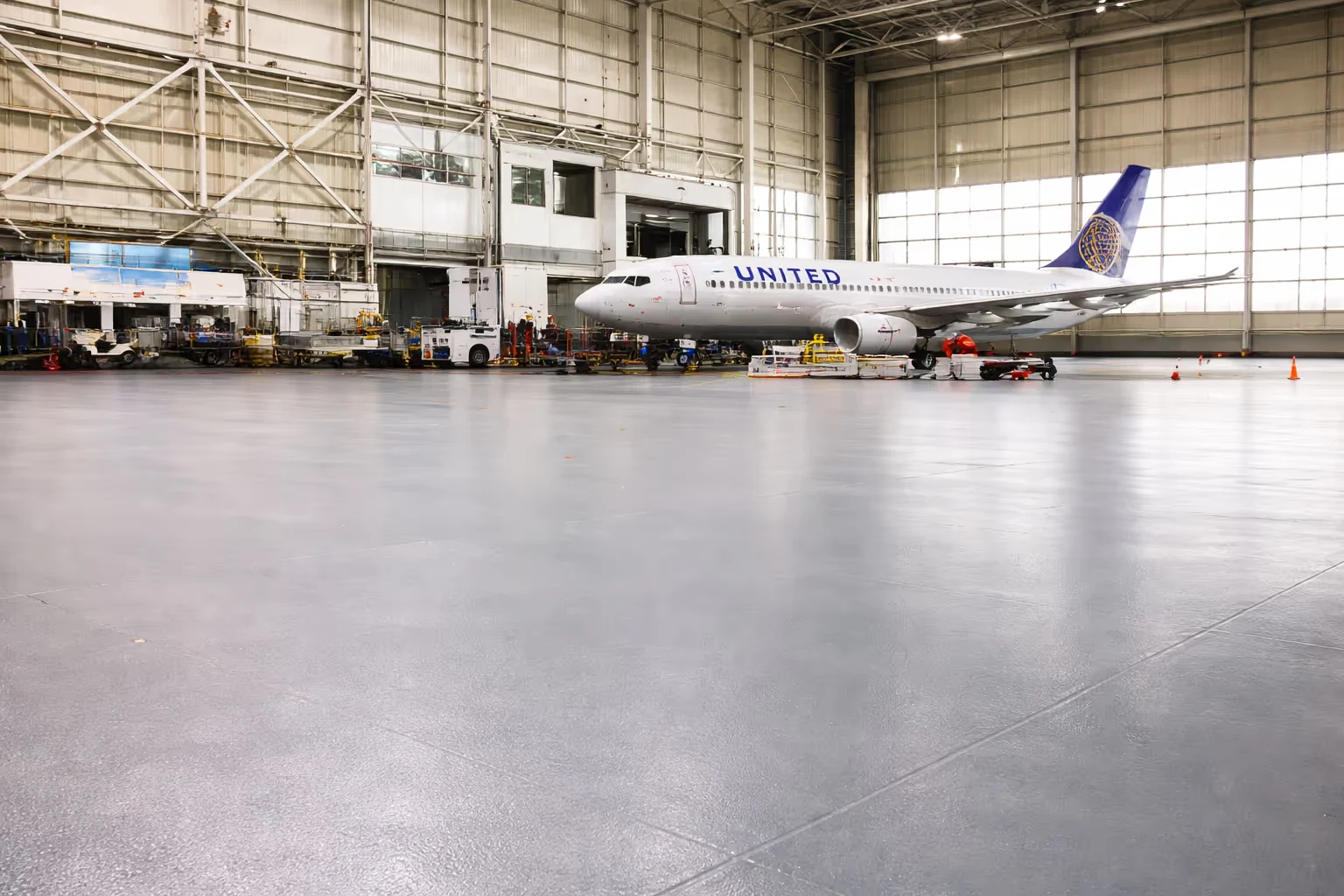 United Airlines airplane parked inside a spacious aircraft hangar with maintenance equipment nearby.