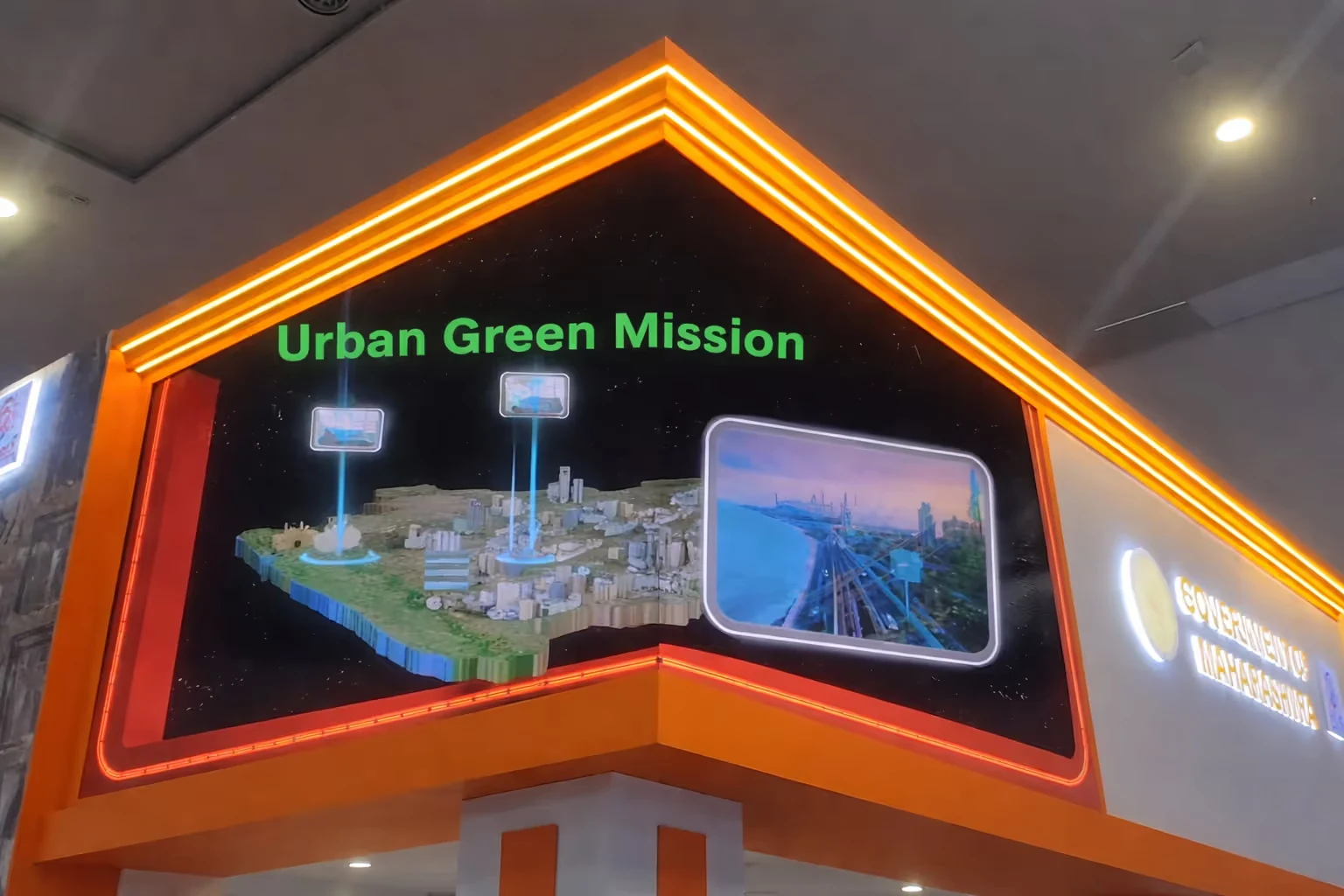 Exhibit corner with a lit-up digital display titled 'Urban Green Mission' featuring a 3D city model and a screen showing an urban landscape.