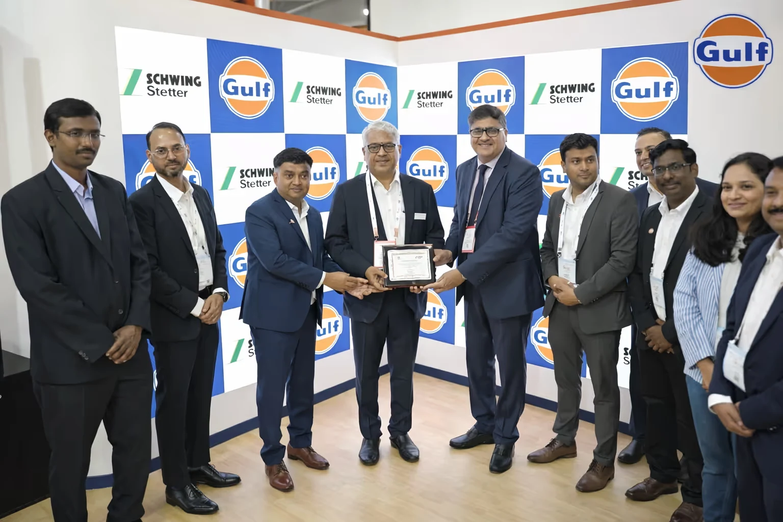 Group of professionals in business attire standing in front of a Gulf and Schwing Stetter branded backdrop holding a certificate plaque.
