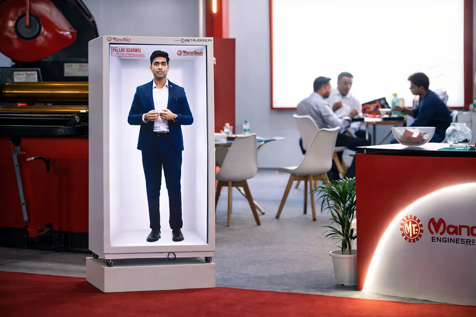 Digital life-sized display of a man in a suit inside a white rectangular frame, at an industrial-style exhibition booth with a few people