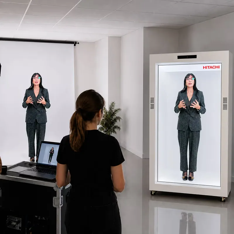 A HoloBox911 operator at a control laptop beside the holographic display unit during the live keynote at the Hitachi corporate event in New Delhi