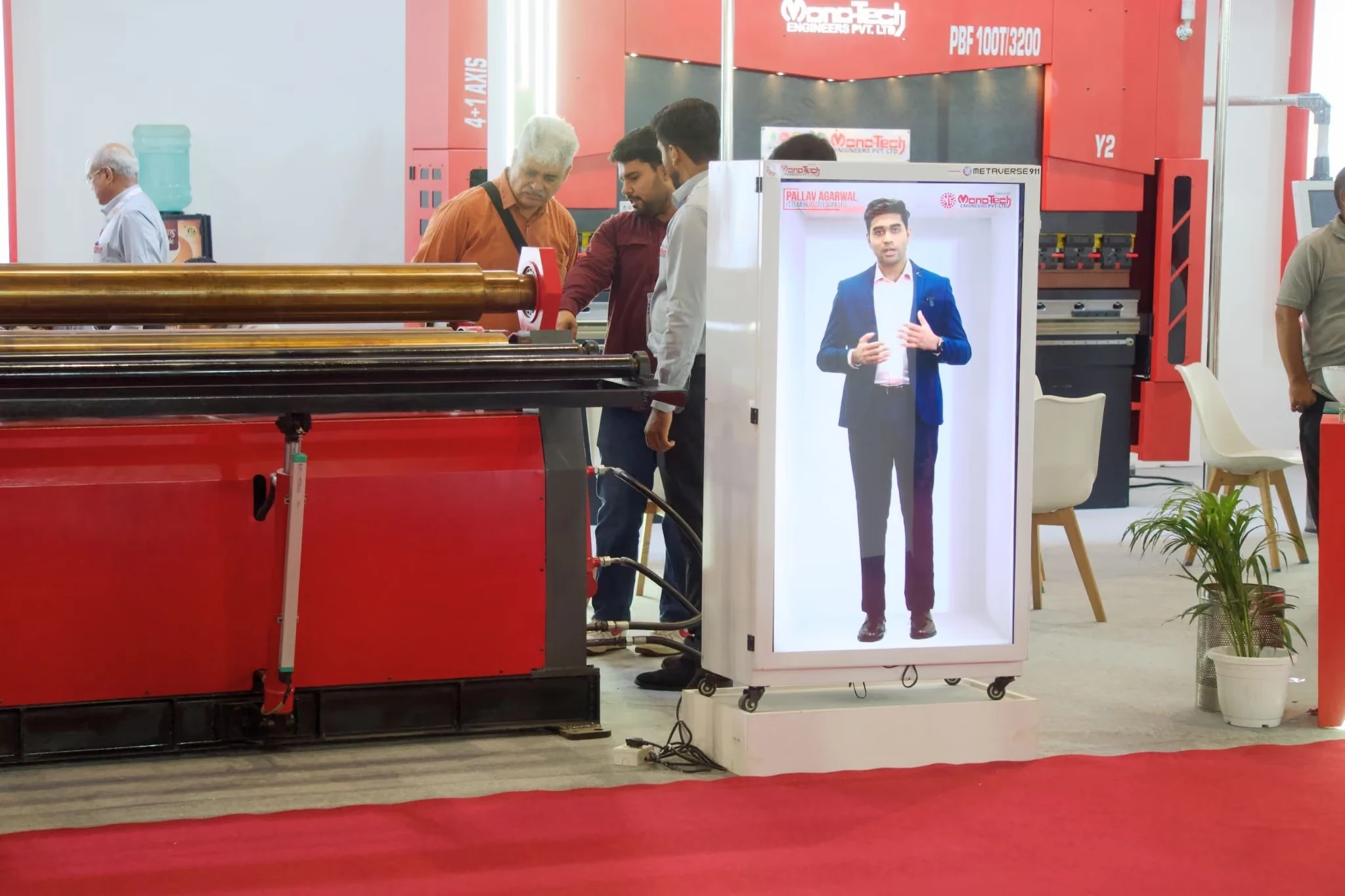Visitors at the Monotech Engineers stand at IMTOS 2025, with the HoloBox911 unit playing the recorded welcome beside red sheet metal