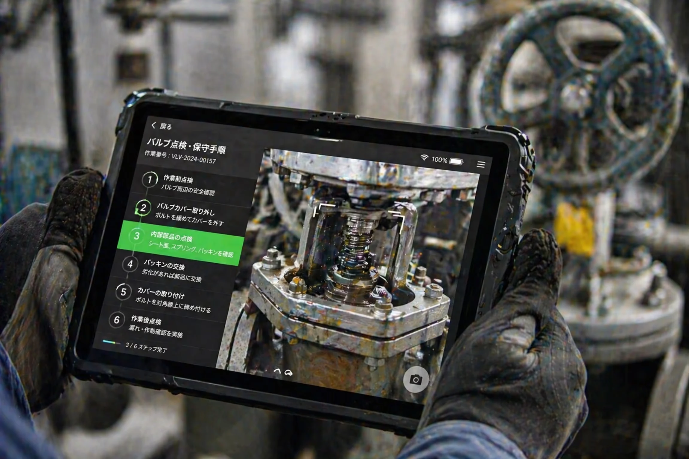 Gloved hands holding a rugged tablet showing detailed Japanese instructions for valve inspection and maintenance, with a close-up image of