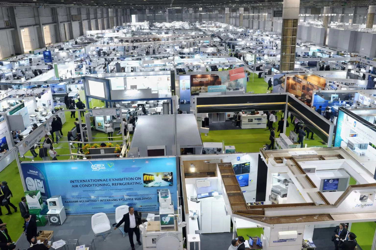 Wide view of a large indoor exhibition hall with numerous booths and attendees walking among them.
